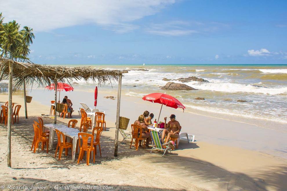 Imagem de turistas no quiosque em uma tarde ensolarada na Praia dos Milionários.
